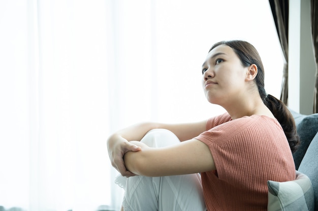 Unhappy asian young woman having a depressed disorder problem\
and living alone in living room. mental health care in young people\
concept.