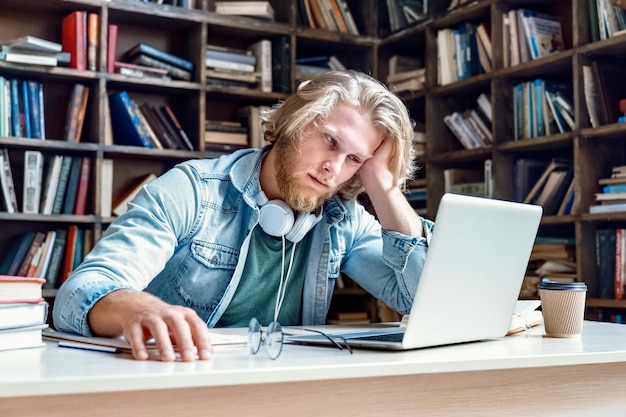 Unhappy bored male student studying looking at laptop