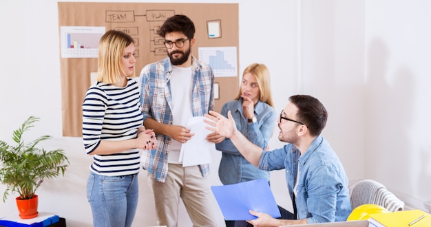 Unhappy boss yelling at the afraid female employee while holding folder with bad results in front of other coworkers.