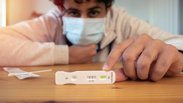 Unhappy caucasian man holding a positive buffer dropper for seft detection of coronavirus at home PCR test after come back from crowd and meeting people Quarantine pandemic