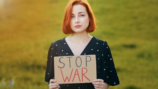 Unhappy caucasian young redhead woman activist hold demonstrating banner with inscription stop war