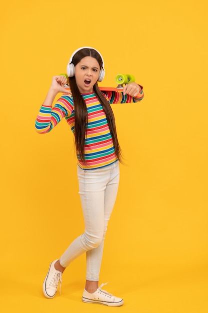 Lo skateboarder bambino infelice ascolta musica in cuffia con hipster da skateboard penny board