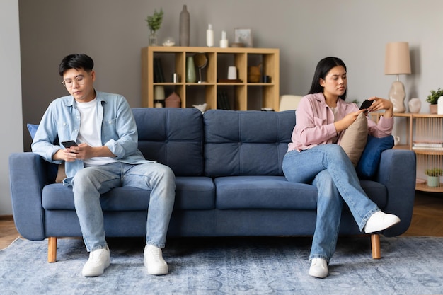 Unhappy chinese spouses sulking and using smartphones sitting at home