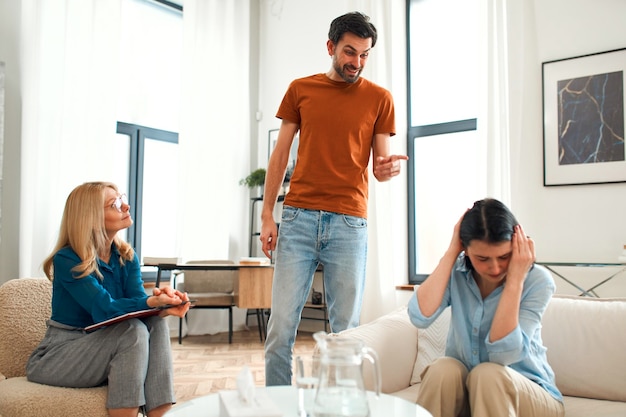 Unhappy couple arguing having fight disagreement at\
psychologists office frustrated young family discussing\
relationship problems with their therapist