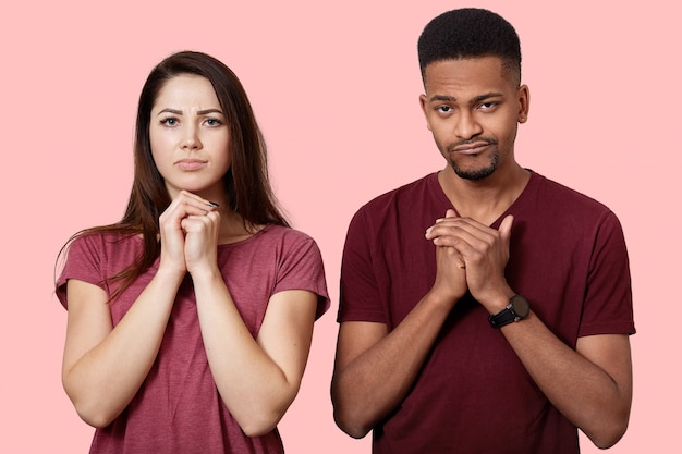 Unhappy couple of different race stand with folded hands