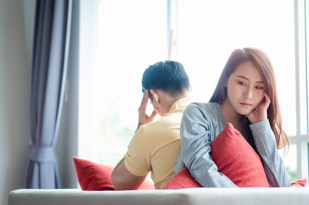 Unhappy Couple sitting behind each other on the couch and avoid talking