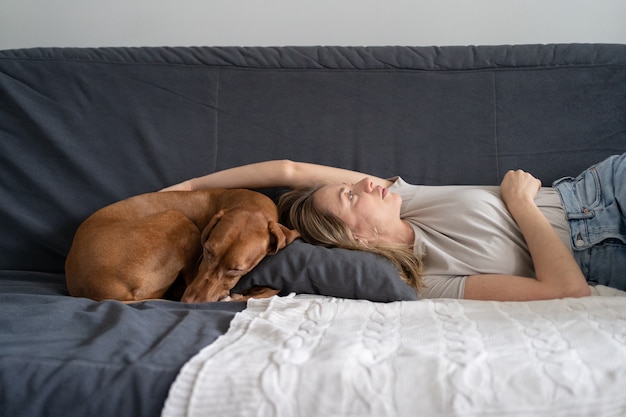 Unhappy depressed woman lying with dog at home on sofa feels apathy has mental problems. Loneliness