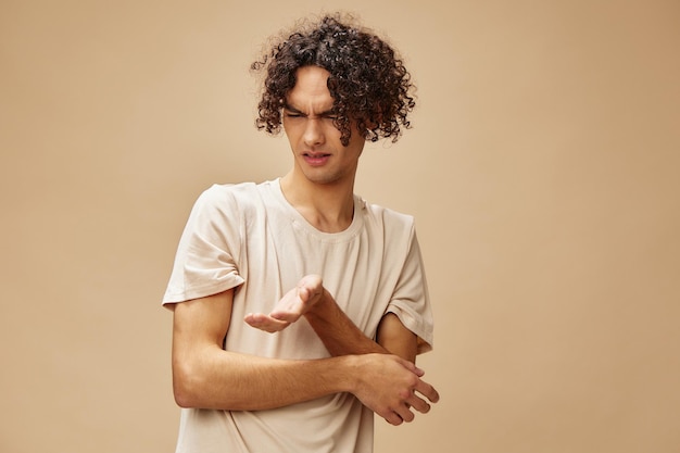 Unhappy discontented awesome tanned curly man in basic tshirt with disgust looks aside posing isolated on beige background Fashion New Collection offer People Emotions concept Free place for ad