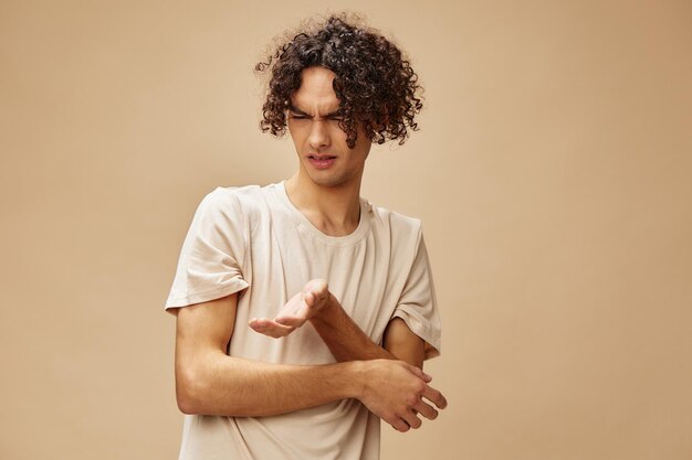 Photo unhappy discontented awesome tanned curly man in basic tshirt with disgust looks aside posing isolated on beige background fashion new collection offer people emotions concept free place for ad