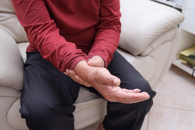 Unhappy elderly man holding his wrist suffering from severe pain in his hand and massaging his achi