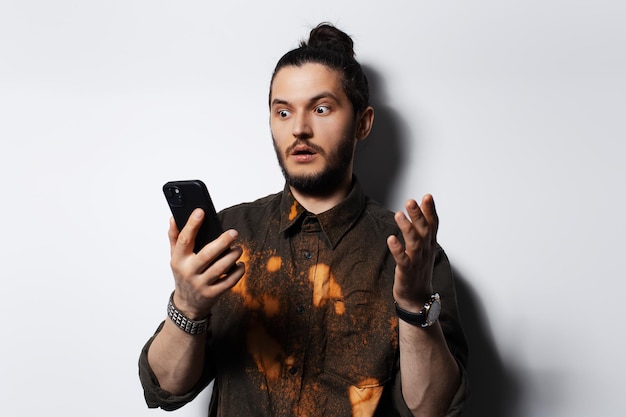 Несчастный хипстерский мужчина удивленно смотрит в смартфон на белом фоне