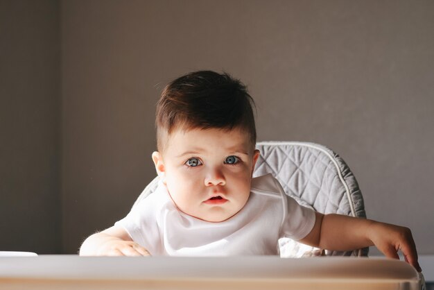 不幸な小さな子供が椅子に座って食べています。小さな椅子に座っている悲しくて不幸な子供。早朝に動揺した幼児の男の子