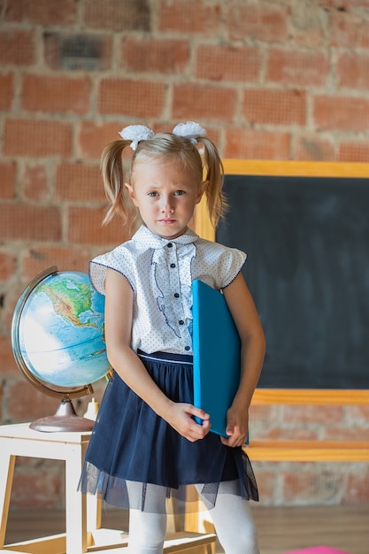 Unhappy little girl in school uniform with a book in her hands, back to school concept