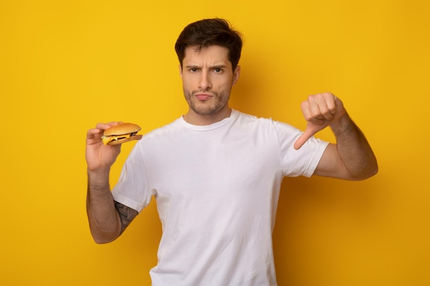 Unhappy man holding burger showing thumbs down