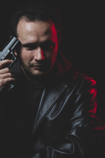 Фото Несчастный, человек с намерением совершить самоубийство, пистолет и кожаная куртка, красная подсветка
