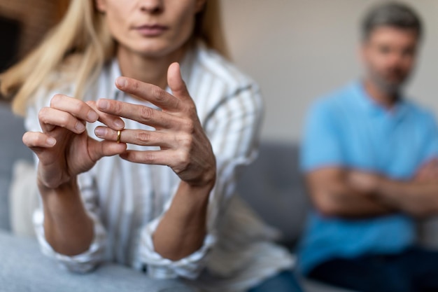 不幸な中年のヨーロッパの女性は、リビング ルームのインテリアで喧嘩中に男を無視してリングを脱ぐ