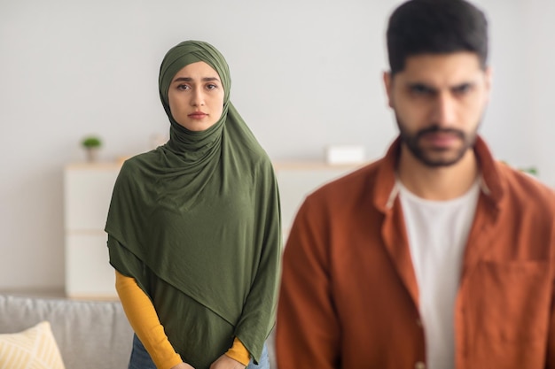 家に戻って夫の後ろに立っている不幸なイスラム教徒の妻