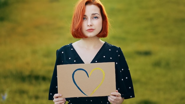 Unhappy redhead woman hold artwork colorful cardboard drawing blue yellow love shape heart romantic