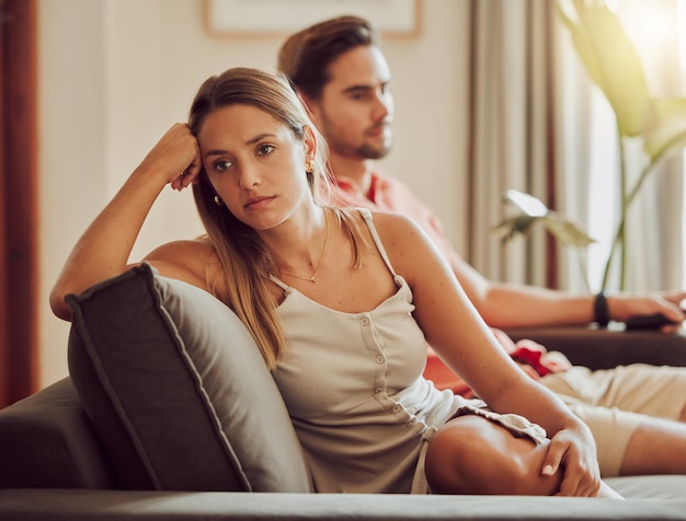 Unhappy sad and annoyed couple after a fight and are angry at\
each other while sitting on a couch at home a woman is stressed\
upset and frustrated by her boyfriend after an argument