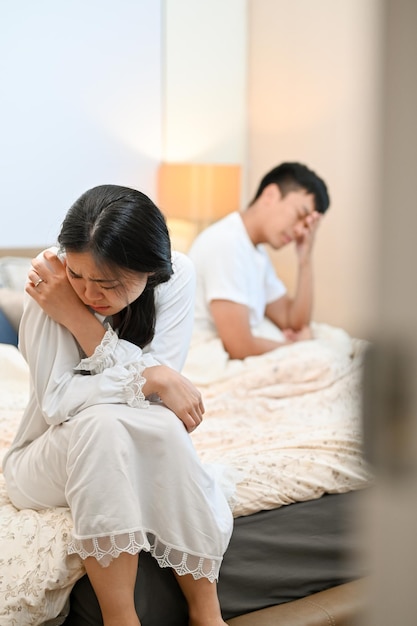 An unhappy sad Asian wife is sitting on the bed and crying after an argument with her husband