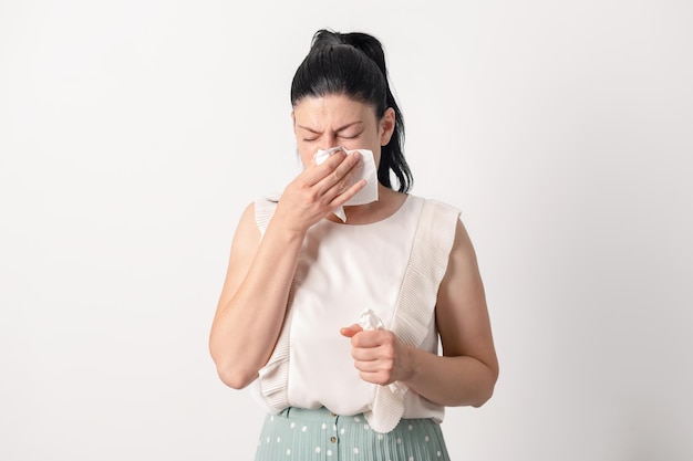 Unhappy sad young female suffering from fever and flu blowing nose in napkin isolated on white