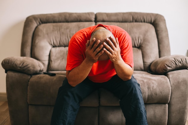 Фото Несчастный напряженный мужчина, держащийся за голову, сидит дома на диване и думает о проблемах