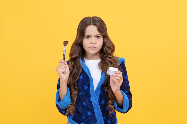 Unhappy teen girl hold powder brush. kid cosmetology and beauty. child in pajama or bathrobe use cosmetics. morning grooming. skincare and makeup. concept of natural beauty.