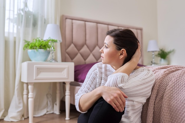 Unhappy tired depressed mature woman sitting at home on the floor