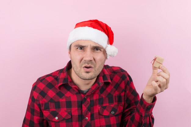 Unhappy, upset man in a red hat, holds a small gift with disgust on his face