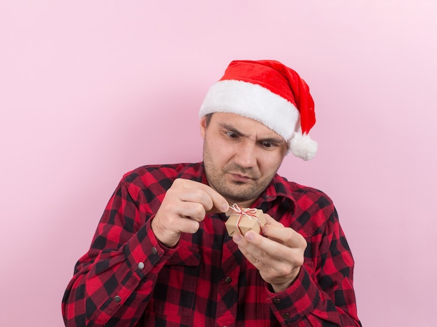 Unhappy, upset man in a red hat, holds a small gift with disgust on his face