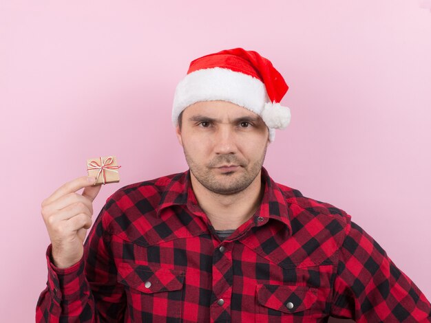 Unhappy, upset man in a red hat, holds a small gift with disgust on his face