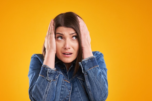 unhappy woman in denim jacket posing over yellow background