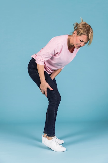 Photo unhappy woman holding her sore thigh muscles on blue background