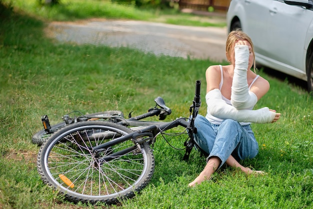 An unhappy woman is sitting with bandaged hands near a bicycle after a fall