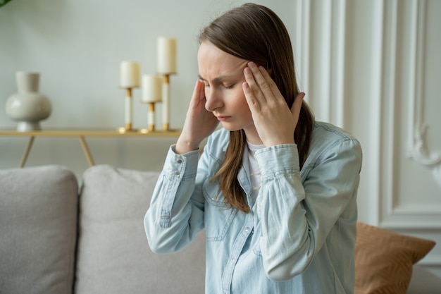 Unhappy woman suffering from head ache at home sitting on the couch