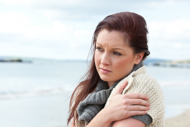 Unhappy woman wearing sweater on the beach and getting cold