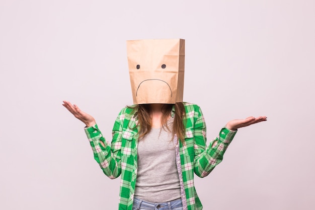 Unhappy woman with sad emoticon in front of paper bag on her head on white background