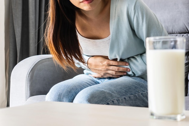 Giovane donna asiatica infelice che ha mal di stomaco con un bicchiere di latte sul tavolo concetto di allergia alimentare intolleranza al lattosio close up copy spacex9