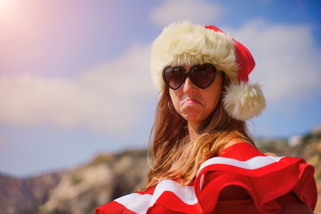 ビーチのクリスマス休暇に赤い水着とサンタの帽子で不幸な若い魅力的なブルネットの女性