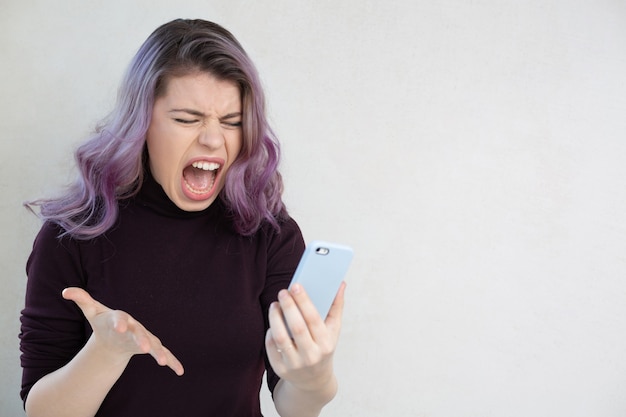 Unhappy young casual dressed woman screaming to the mobile phone screen. Empty space