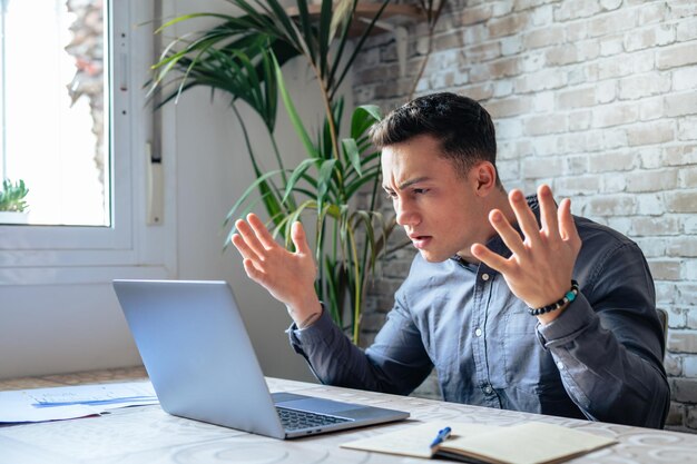 写真 眼鏡をかぶった不幸な若い白人男性労働者がノートパソコンの画面を見てショックを受けました