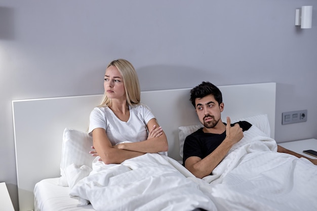 불행한 젊은 백인 여성과 수염 난 남자가 집에서 침대에서 말다툼을 한 후 말을 하지 않는다.