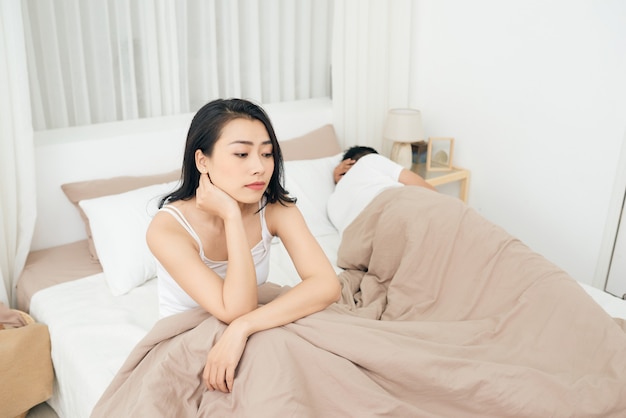 Unhappy Young Couple Sitting On Bed In Bedroom