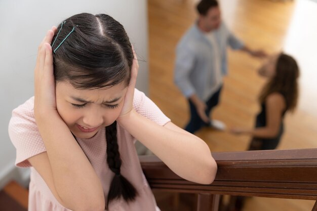 Unhappy young girl watch her parent arguing from the stair Synchronos