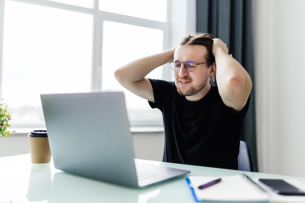 Il giovane lavoratore infelice con gli occhiali guarda lo schermo del laptop scioccato dal guasto del gadget o da problemi operativi uomo frustrato confuso sorpreso da un errore imprevisto sul dispositivo del computer