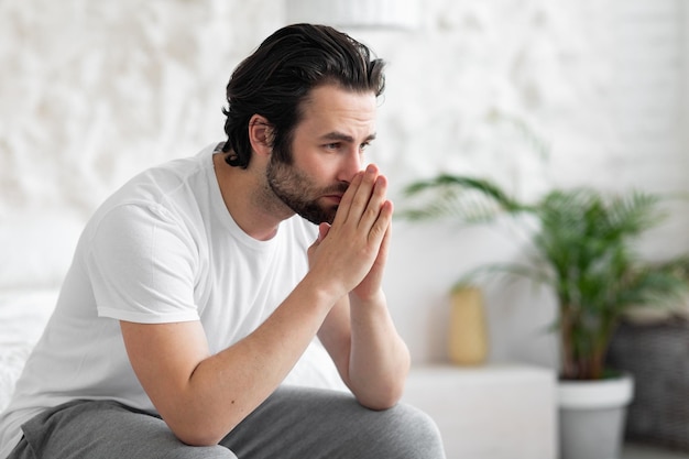 Unhappy young man sitting on bed alone copy space