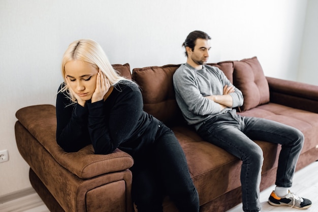 Unhappy young wife and husband not talking after quarrel sitting on couch at home 