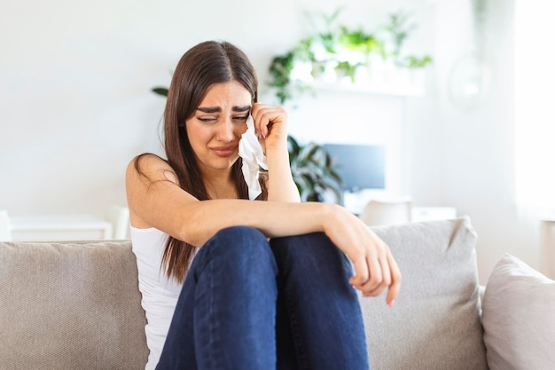 Photo unhappy young woman covering face with hands crying alone close up depressed girl sitting on couch at home health problem or thinking about bad relationships break up with boyfriend divorce