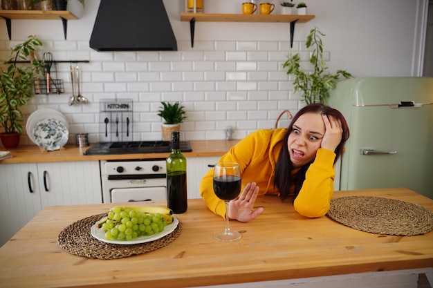 Unhappy young woman has headache from red wine Adult female feels bad from alcohol while in kitchen