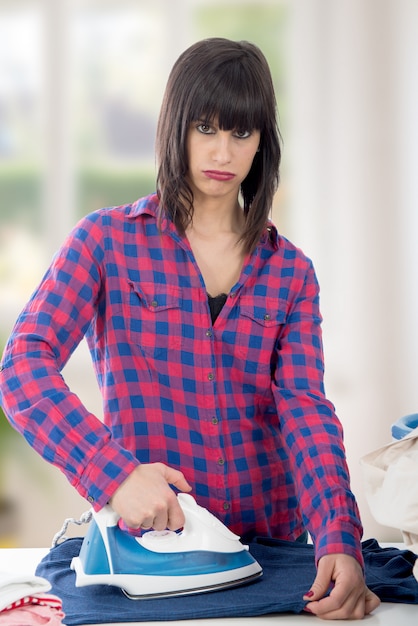 Unhappy young woman ironing clothes